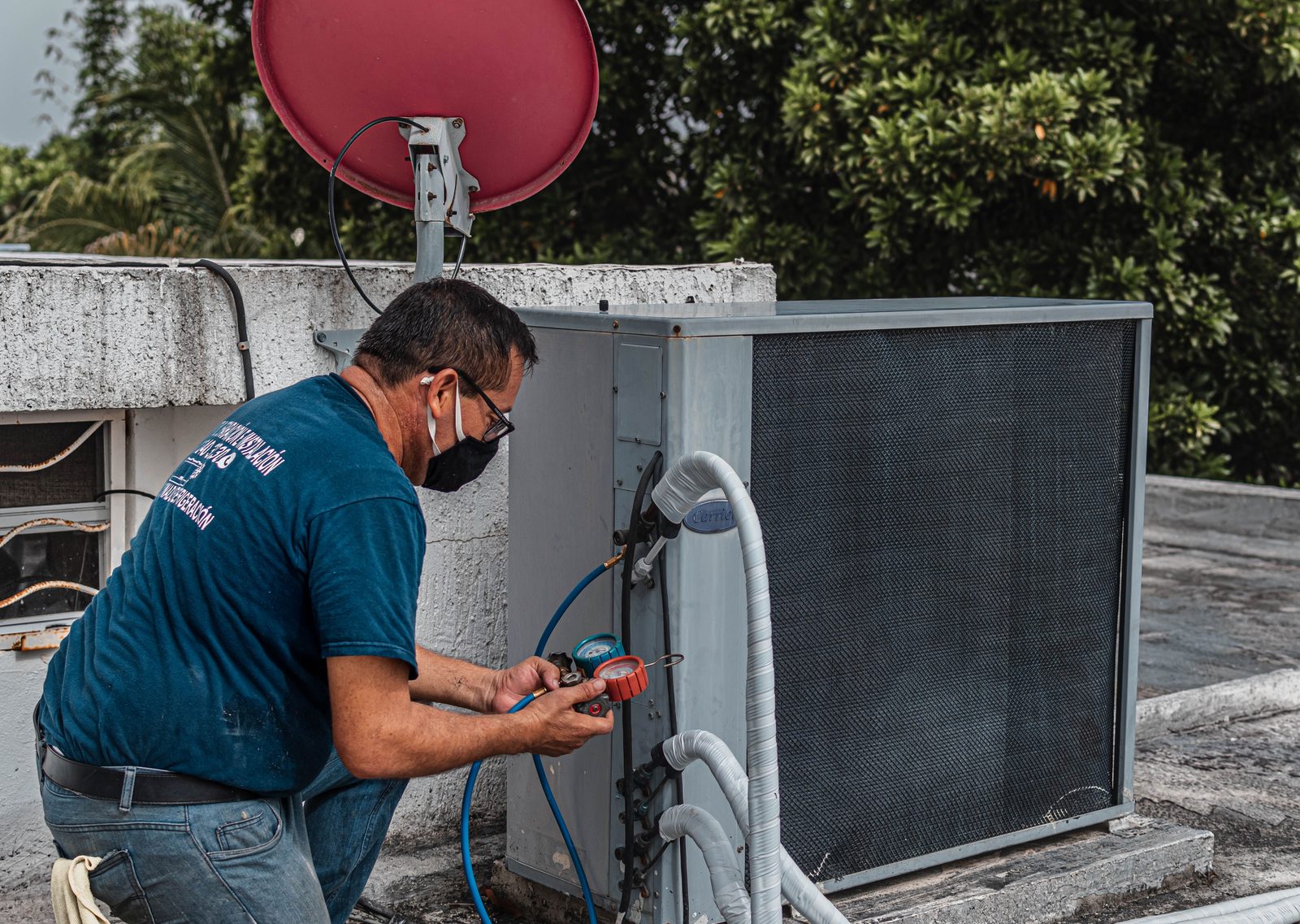 Technician in a mask connecting gauges to an outdoor air conditioner
